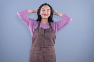 Elleri başının arkasında, gözleri kapalı, mor gömlekle gülümseyen bir kadın.