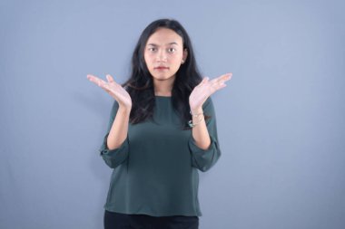 Genç bir Asyalı kadın açık avuçlarıyla omuz silkiyor, belirsizliğini dile getiriyor ya da 