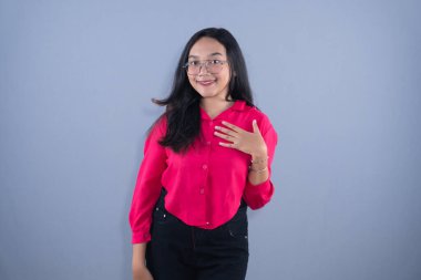 Young Asian woman in a pink shirt and glasses, smiling with hand on chest