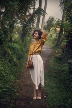 Palmiye ağaçlarıarasındaki yolda beyaz elbiseli bir kız. Bali gezisi. Seyahat, macera.