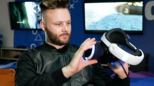 Młody człowiek patrzy na okulary wirtualnej rzeczywistości, trzymając je w ręce — Wideo stockowe