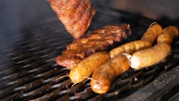 De kok blijkt de gegrilde varkensribbetjes en worstjes met metalen tangen. Onder het raster gaat rook. — Stockvideo