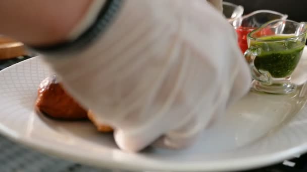 Готовка тщательно регулирует приготовленные сосиски на тарелке рядом с различными соусами. Мясо барбекю — стоковое видео