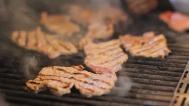 Eti biftek bir gaz ızgarada pişirilir. Açık havada lezzetli et yemekleri. Duman gıdalardan giriyor. Cook beef metal maşa ile döner..