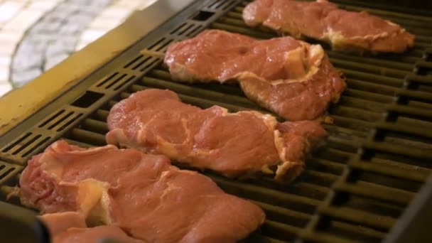 Grandes filetes de carne cruda se tuestan en la rejilla de la parrilla de gas. Un pequeño humo viene del plato. Barbacoa en equipo profesional. Cocinar alimentos poco saludables al aire libre . — Vídeos de Stock