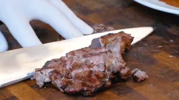 Heerlijke, sappige, vers gekookt vlees steaks cook snijdt en verwijdert stukken uit de snijplank op plaat. SAP uit de steaks blijft op het bord. Vette gezonde voeding met een grill. Close-up van video. — Stockvideo