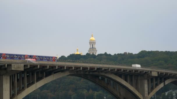 Trein rijdt over de brug tegen de hemel en de koepels van de kerk. Metro blijven buiten. Openbaar vervoer in beweging. Auto's gaan over de brug over de rivier. — Stockvideo