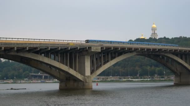 Le train traverse le pont contre le ciel et les coupoles de l'église. Métro de la ville à gauche. Transports publics en mouvement. Voitures passer sur le pont sur la rivière . — Video