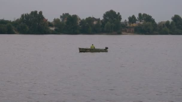 Pescador em um pequeno barco velho no meio do rio está pescando por uma isca. Lazer e hobby de um homem desconhecido. Litoral e árvores no fundo . — Vídeo de Stock