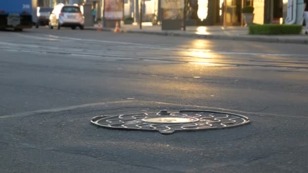 道路上の古いマンホール。夕暮れ時のうるさい街。カメラの前で道を通って車がいくつか。トラムは、太陽の反射をブロックします。 — ストック動画