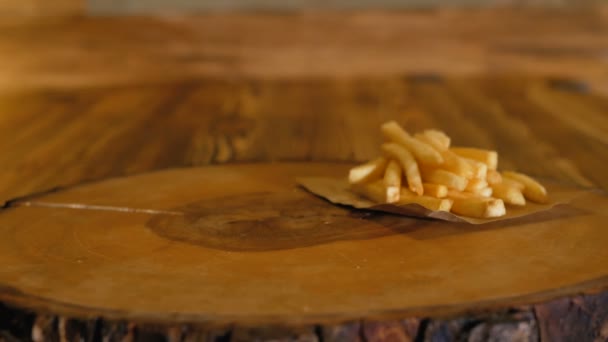 Mãos em luvas colocar um hambúrguer preto suculento com grandes costeletas e legumes na tábua de madeira ao lado das batatas fritas. Comida rápida não saudável . — Vídeo de Stock