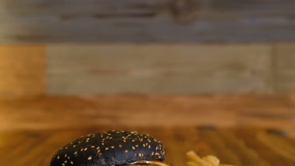 Zwarte hamburger met grote kotelet en fruit ligt op een stuk hout. Ongezonde voeding. Professioneel gekookte fastfood. — Stockvideo