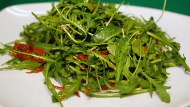 Rucola-Salat und getrocknete Tomaten rotieren auf einem weißen Teller. gesunde Ernährung aus nächster Nähe. Ungewöhnliche Rezeptgerichte. — Stockvideo