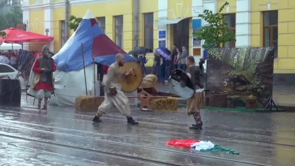 Βινία Ουκρανία-18 Μαΐου, 2019: μια γυναίκα και ένας άντρας με ένα άλογο που πάλεψε με σπαθιά και ασπίδες σε έναν δρόμο της πόλης. Σκηνοθετημένο σε ένα φεστιβάλ της πόλης κατά τη διάρκεια της βροχής. — Αρχείο Βίντεο