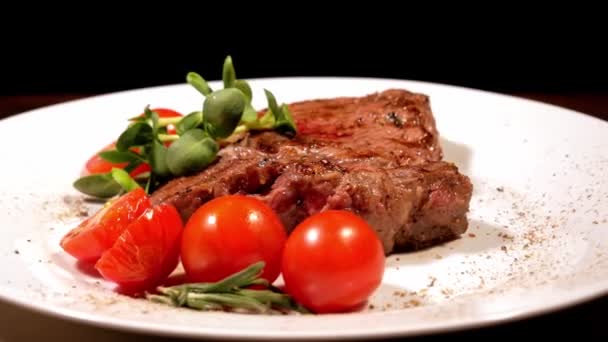 Een stuk gebakken vlees gegarneerd met cherry tomaten en micro groente roteren op een witte plaat. Smakelijke gegrilde biefstuk close-up. — Stockvideo