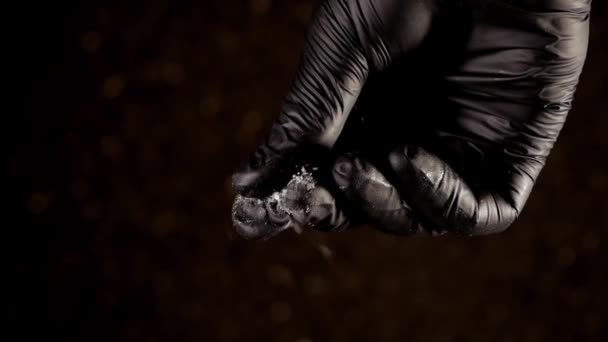Hand in schwarzem Handschuh streut Salz in Zeitlupe herunter. — Stockvideo