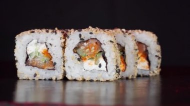 Suşi ruloları siyah arka planda döner. Yakın plan çekim. Japon yemeklerinde Philadelphia peyniri ve somon balığı.
