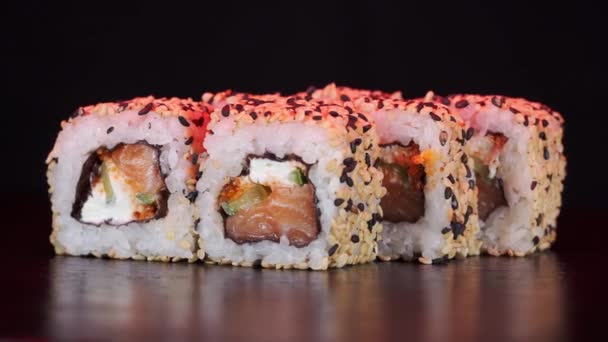 Rolki sushi obracają się na czarnym tle. Zdjęcia z bliska. Filadelfijski ser i łosoś w japońskim jedzeniu. Czerwone światło. — Wideo stockowe