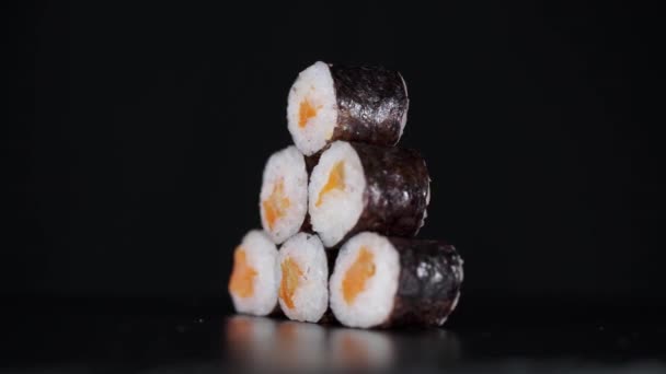 A sushi piramis formájú tekercsek fekete alapon forognak. Közelről lőtték le. Lazac a japán ételekben. — Stock videók
