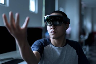 Laboratuvarda VR gözlükleriyle gerçeği karıştırmaya çalışan Asyalı genç bir öğrenci. Sanal gerçeklik kulaklığı kullanırken erkeklerin hareketi