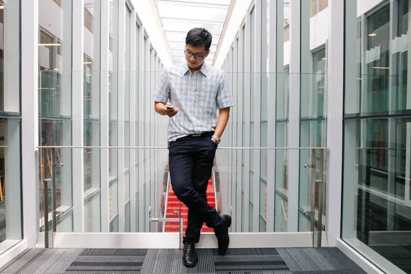 Schöner Asiatischer Junge Checkt Sein Smartphone Auf Dem Flur lizenzfreie Stockfotos