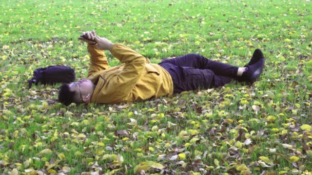 Sám muži se žlutou bundou pomocí smartphonu v parku podzimu. — Stock video