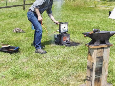 Bahçedeki örs üzerinde demir çalışan bir tanımlanamayan demirci adam.