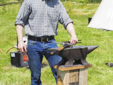 Bahçedeki örs üzerinde demir çalışan bir tanımlanamayan demirci adam.