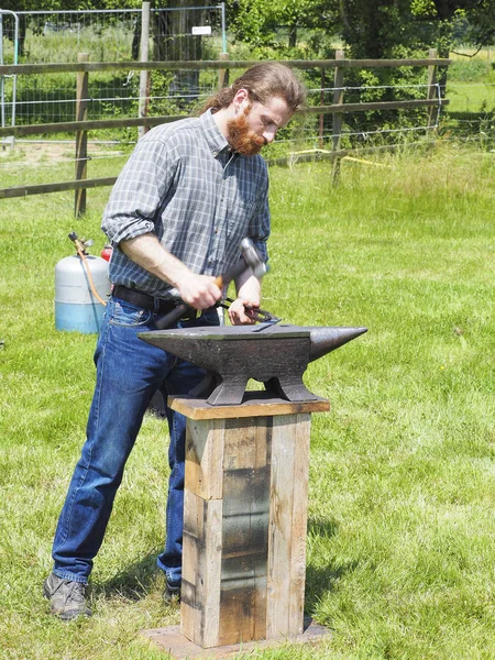 Belgesel yayın görüntü. Elbeuf, Fransa - 9 Haziran 2018. Bahçedeki örs üzerinde demir çalışan bir tanımlanamayan demirci adam.