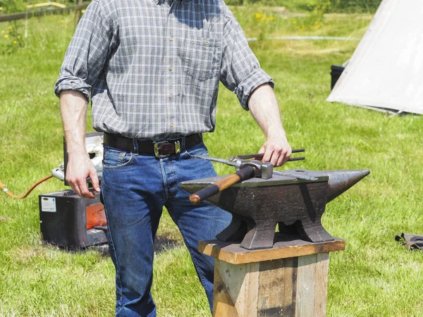 Bahçedeki örs üzerinde demir çalışan bir tanımlanamayan demirci adam.