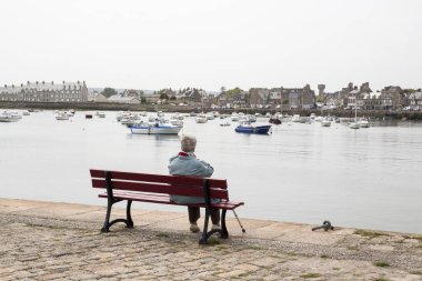 Barfleur, Fransa - Haziran yaklaşık, 2018. O deniz ve tekne manzarayı izliyor gibi yaşlı bir kadın kıdemli bir bankta oturur. Yalnızlık üst düzey insanlar kavramının