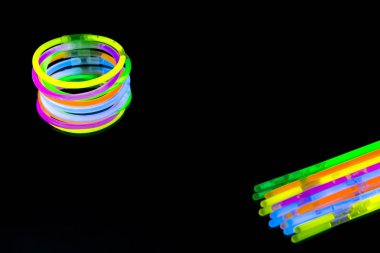 Renkli floresan ışık neon glow stick Bileklik kayış Bileklik ayna yansıması siyah arka plan üzerinde. Sarı mavi pembe turuncu yeşil mor kızdırma sopa