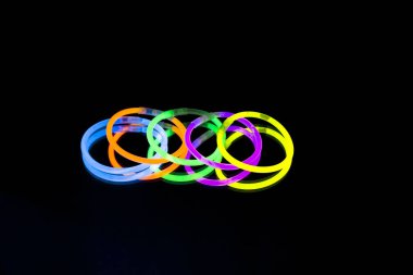 Renkli floresan ışık neon glow stick Bileklik kayış Bileklik ayna yansıması siyah arka plan üzerinde. Sarı mavi pembe turuncu yeşil mor kızdırma sopa