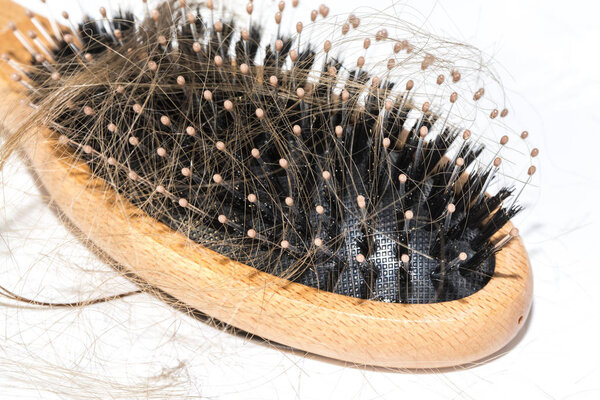 Hair loss on washbasin. Long brown hair with wood brush on white basin in the bathroom. Healthcare concept