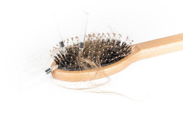 Wood hairbrush on white background. Close-up with long brown hair and syringe to illustrate hair loss treatment medicine. Hair loss problem. Health care concept.