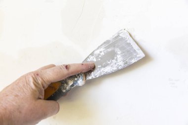 Bir kadın elinin alçı dolgu duvara eski metal spatula ile yakın çekim