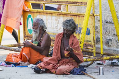 Yaklaşık, rameshwaram, Pamban Adası, Tamil Nadu, Hindistan - 2018 Mart. Bir grup kimliği belirsiz Sadhus hacı Gıda için bekleyen road, sokakta oturan Turuncu elbise giymiş. Bu inanç bir kitle Hindu Hac ve Kutsal içinde banyo