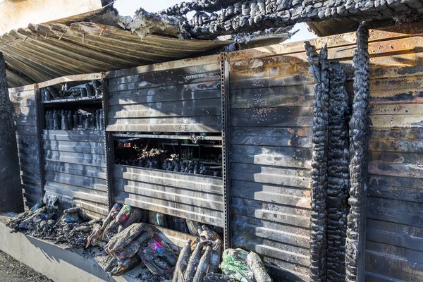 Close up damaged industry supermarket metallic facade after arson fire with burn debris of plastic beer bottle after intense burning fire disaster ruins waiting for investigation for insurance.
