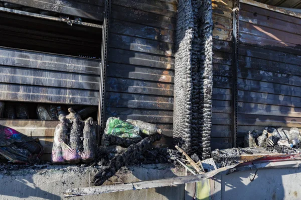 Close up damaged industry supermarket metallic facade after arson fire with burn debris of plastic beer bottle after intense burning fire disaster ruins waiting for investigation for insurance.