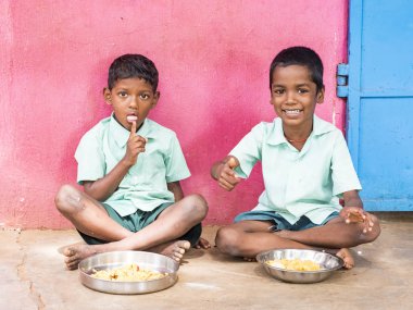 Puducherry, Tamil Nadu, Hindistan - Aralık yaklaşık, 2018. Bazı masala ile pirinç onların sağ eli ile yemek iki kimliği belirsiz zavallı sınıf çocuklar yere dış üzerinde oturan üniformalar. Öğle yemeği zamanı, genel hükümet okulda sağlıksız gıda