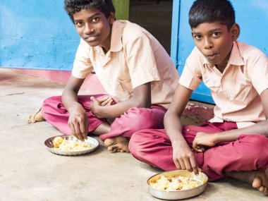 Puducherry, Tamil Nadu, Hindistan - Aralık yaklaşık, 2018. Bazı masala ile pirinç onların sağ eli ile yemek iki kimliği belirsiz zavallı sınıf çocuklar yere dış üzerinde oturan üniformalar. Öğle yemeği zamanı, genel hükümet okulda sağlıksız gıda