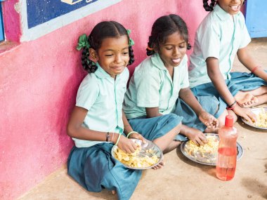 Puducherry, Tamil Nadu, Hindistan - Aralık yaklaşık, 2018. Bazı masala ile pirinç onların sağ eli ile yemek tanımlanamayan zavallı sınıf kızlarla yerde açık havada üzerinde oturan üniformalar. Öğle yemeği zamanı, genel hükümet okulda sağlıksız gıda
