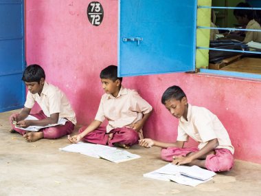 Puducherry, Hindistan - Aralık yaklaşık, 2018. Hükümet tanımlanamayan mutlu konsantre çocuklar sınıf okul katta oturan, açık havada kitaplarla eğitim üniformaları. Dostluk duygu zevk okul çocuk portresi.