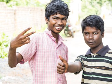 Puduchery, Hindistan - Aralık yaklaşık, 2018. Kameraya, seyir iki kimliği belirsiz gençler Asya Hint iki erkek fakir köy sokakta göstermek uzakta, zafer parmakları ile işaret yapma.