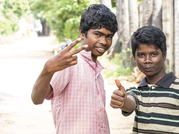PUDUCHERY, INDIA - DECEMBER Circa, 2018. Two unidentified teenagers asian indian two boys looking at camera, making victory sign with fingers, showing off, in the street of poor village.