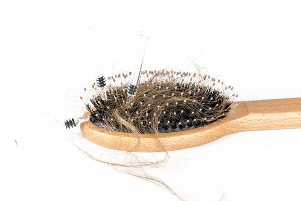Wood hairbrush on white background. Close-up with long brown hair and syringe to illustrate hair loss treatment medicine