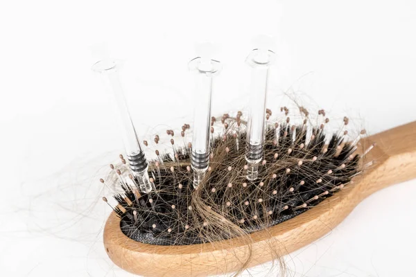 Escova de cabelo de madeira no fundo branco. Close-up com cabelos castanhos longos e seringa para ilustrar a medicina de tratamento de perda de cabelo — Fotografia de Stock