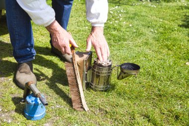 Koruyucu giysiler içinde arıcı eli çim bahçede fırça ile eski sigara içen açma.