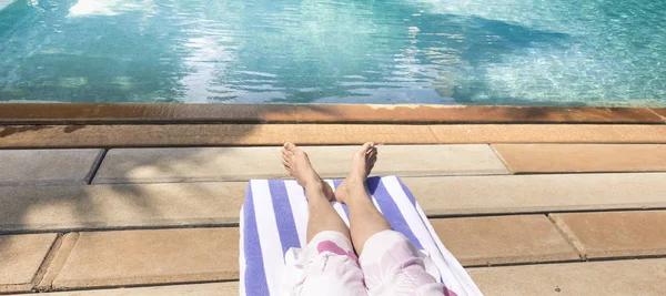 Bare feet of young lady lying on deck chair sunbathing by the swimming pool.