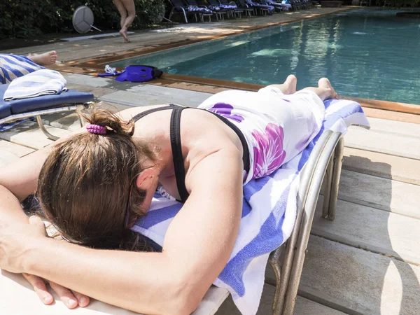 Pés descalços de jovem deitada na espreguiçadeira tomando banho de sol na piscina . — Fotografia de Stock